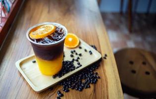 menu de bebida de café gelado laranja americano com frutas frescas de laranja misturadas em um copo de plástico no balcão de madeira do café foto