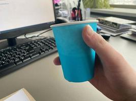 xícara de café azul de papelão de uma cafeteria em uma área de trabalho com um computador com teclado e mouse e material de escritório de um trabalhador de escritório durante o almoço. pausa para café de negócios foto