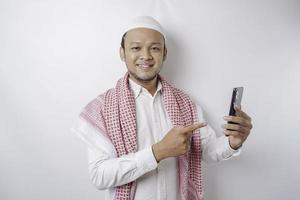um retrato de um homem muçulmano asiático feliz sorrindo enquanto segura seu telefone, isolado pelo fundo branco foto