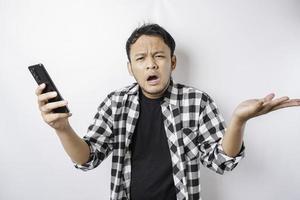 um jovem asiático insatisfeito parece descontente vestindo camisa xadrez expressões faciais irritadas segurando seu telefone foto