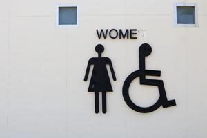 sinal preto de mulher e banheiro de cadeira de rodas no edifício de concreto de parede branca foto