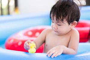 retrato de bebê de 1 a 2 anos. menino jogando pato amarelo de borracha. criança jogando água na piscina. na temporada de verão. tempo de atividade feliz. as crianças brincam na água para se refrescar do clima. espaço vazio. foto