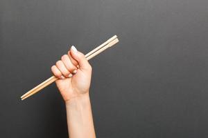 a mão de uma mulher segurando os pauzinhos em fundo preto. conceito de comida chinesa com espaço vazio para seu projeto foto