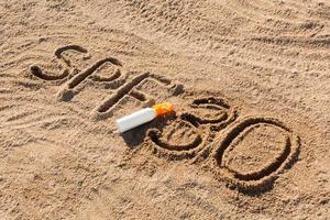 protetor solar fator trinta. palavra spf 30 escrita na areia e garrafa branca com creme bronzeador. fundo de conceito de cuidados com a pele foto