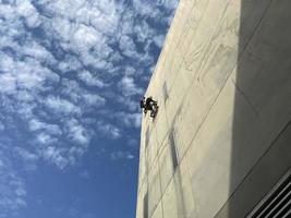 pintor consertando a parede e pintando na parede do trabalhador da construção civil com uma escova de rolo trabalho em edifícios altos sem equipamento de segurança o conceito de trabalho perigoso em altura foto