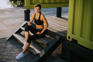 bela jovem fazendo uma pausa durante o exercício fora e usando o celular foto