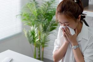 empresária asiática espirrando por causa de um resfriado no escritório. conceito de cuidados de saúde. foto