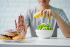 jovem mulher rejeitando junk food ou alimentos pouco saudáveis, como rosquinhas e escolhendo alimentos saudáveis, como maçã verde e salada para sua saúde. foto