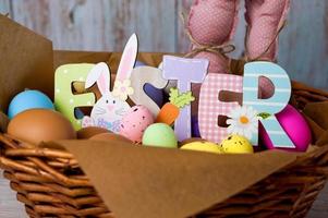 closeup da cesta de páscoa com ovos coloridos, toy bannies anf placa de madeira de páscoa. foto