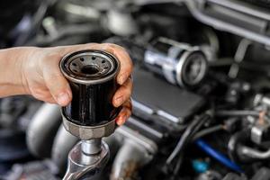 feche o filtro de óleo antigo do carro e a chave na mão um homem muda no conceito de serviço da sala de máquinas do carro foto