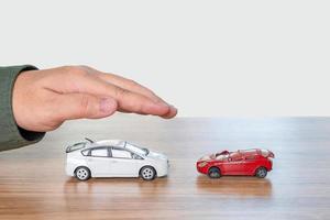 comparações do conceito de acidente em carro de uso, carro de brinquedo em perfeitas condições com proteção de mão e homem e compare os carros de brinquedo danificados na mesa e fundo branco foto