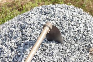 pilha de cascalho de construção ou pedra com enxada no canteiro de obras no calor do sol. foto