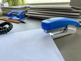 um grande grampeador azul para grampear papel fica ao lado das pastas de documentos na mesa de trabalho do escritório. papelaria foto