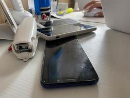 dois telefones celulares com tela sensível ao toque em funcionamento, smartphones estão sobre a mesa no escritório com artigos de papelaria, grampeador, lacre e laptop foto