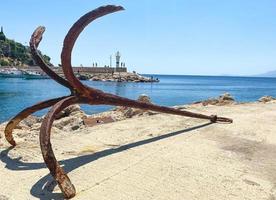 âncora velha e enferrujada à beira-mar. no porto com navios e iates há uma âncora. os turistas podem ver a ferrugem na âncora. a âncora está no asfalto, deixada após um passeio de barco foto