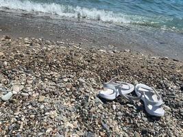 chinelos azuis em uma praia de seixos. temas de verão de praia foto