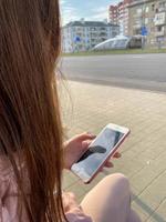 linda menina mulher sentada e segurando um smartphone de celular branco moderno na mão com os dedos com uma bela manicure na rua foto