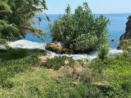 vista legal de cima da borda de um penhasco verde e a costa rochosa acidentada sendo atingida por ondas esmeraldas espumantes. foto impressionante da costa negra e água batendo no penhasco