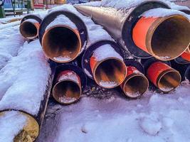 tubos longos, pretos e estreitos para colocar comunicações de encanamento. tubos de metal são cobertos com uma camada de neve. construção, material para trabalhos de reparação foto