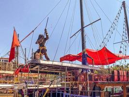 iate turístico atracado na costa. um pirata está de pé no convés e acenando com uma lança. performance para crianças à beira-mar. bandeiras vermelhas em iates foto