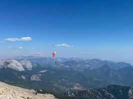 parapente sobre montanhas com pára-quedas. parapente atrás da paisagem de colinas de céu azul. pessoas esportivas turísticas ativas voam usando pára-quedas foto