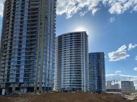 altas grandes belas casas novas modernas edifícios novos arranha-céus feitos de vidro e concreto em um canteiro de obras de uma cidade grande contra um céu azul foto