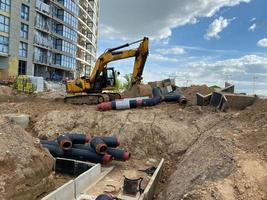 poderosa escavadeira profissional industrial amarela fazendo trabalho de reparo subterrâneo de terraplenagem e enterrando grandes canos de água preta em um canteiro de obras foto