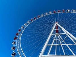 Parque de diversões. roda gigante feita de metal branco. uma enorme roda com cabines para turistas em branco e vermelho. roda gigante contra o céu azul claro foto