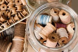 vista superior em pequenas bobinas de madeira em uma cesta e grandes bobinas com fios coloridos em uma jarra de vidro. foto