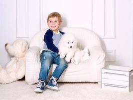 menino sorridente de três anos brincando com cachorrinho branco de samoieda no estúdio foto