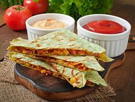 quesadilla mexicano fatiado com legumes e molhos em cima da mesa foto