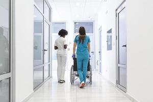 paciente em cadeira de rodas com médica profissional afro-americana e equipe especializada em enfermagem no corredor do centro de recuperação hospitalar foto