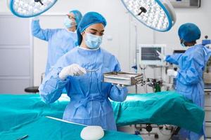 cirurgiã em uniforme cirúrgico levando instrumentos cirúrgicos na sala de cirurgia. jovem médica no teatro de operação do hospital foto