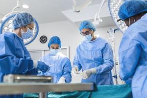 profissionais de saúde multiétnicos realizando cirurgia em paciente no teatro de operação. colegas médicos operando na sala de emergência do hospital. eles estão em esfoliantes foto