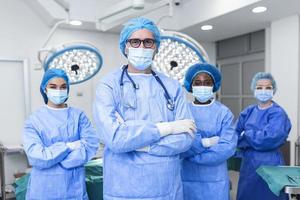 retrato da equipe médica multicultural em pé na sala de operações. retrato de trabalhadores médicos bem sucedidos em uniforme cirúrgico no teatro de operação, pronto para a próxima operação. foto