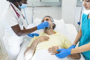 médica conversando com paciente ao longo de colega de trabalho na UTI. homem está deitado na cama entre trabalhadores essenciais. os profissionais de saúde estão em roupas de trabalho de proteção. foto