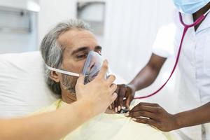 homem sênior recebendo uma máscara de oxigênio do médico para ajudá-lo a respirar melhor durante a crise de saúde do coronavírus covid-19. medicina clínica privada ou tratamento hospitalar foto