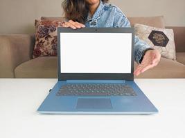 laptop de maquete. mulher asiática mostrando novo modelo de laptop para recomendar conselhos de compra em jaqueta jeans casual na mesa branca foto