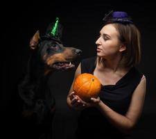 retrato de um cachorro doberman com uma dona de menina. em fantasias de carnaval com uma abóbora. foto