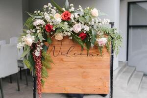 uma placa de boas-vindas com uma bela decoração de flores, em frente à entrada do casamento. foto