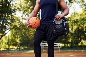 belas árvores verdes no fundo. homem afro-americano joga basquete na quadra ao ar livre foto