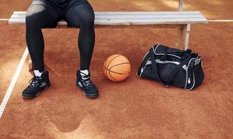 senta-se com bolsa preta e se preparando para o jogo. homem afro-americano joga basquete na quadra ao ar livre foto