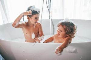 duas crianças se divertindo e se lavando no banho em casa foto
