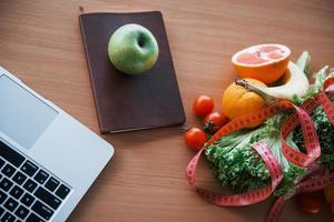 vista superior de alimentos saudáveis, fita métrica e laptop em cima da mesa. concepção de cuidados de saúde foto