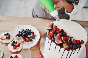 close-up vista da mulher derramando creme na torta na cozinha foto