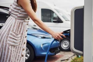 mulher na estação de carga de carros elétricos durante o dia. veículo novo foto