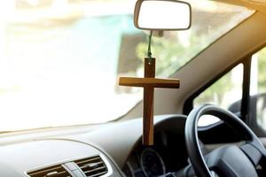 closeup crucifixo de madeira pendurado no volante dianteiro e console do carro. conceito, talismã, amuleto para evitar acidentes. crença, fé, santo em Deus para proteger ao dirigir.