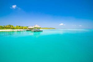 bela praia tropical nas maldivas com poucas palmeiras e lagoa azul. molhe e villa de água com fundo de resort de ilha paradisíaca foto