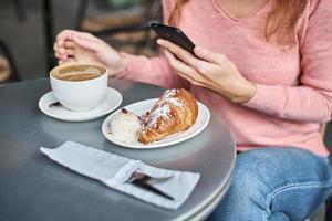 mulher toma café da manhã no café e usa smartphone. foto