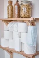 estoques de rolos de papel higiênico, máscara protetora e produtos na prateleira em casa foto